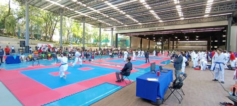 Large indoor judo competition with multiple blue and red mats, instructors, and young athletes in white gis competing in a covered arena.