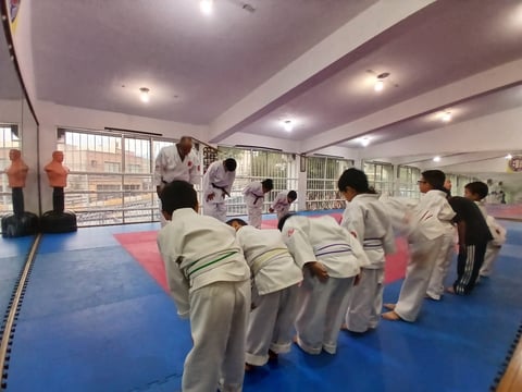 Children in white martial arts uniforms training on blue and red mats in an indoor dojo with an instructor demonstrating techniques