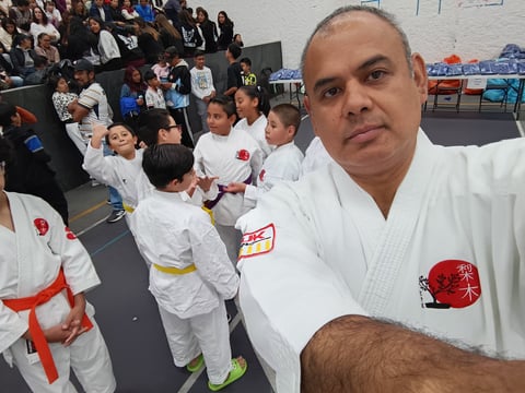 Instructor in white karate gi taking selfie with young martial arts students in background during class training session
