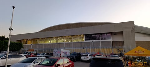 Modern curved warehouse building with parking lot, vehicles, and yellow tent in foreground under clear sky