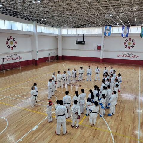 Group of martial arts students in white uniforms standing in a circle during training in a gymnasium with wooden flooring