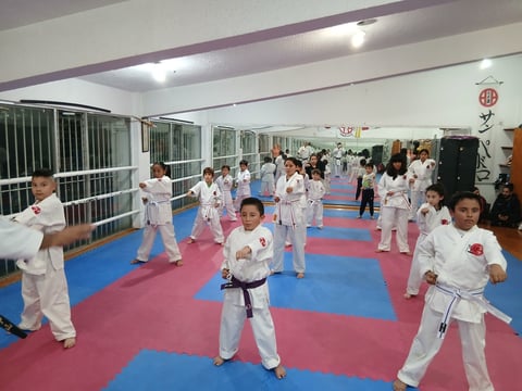 Children in white karate uniforms practicing on a red and blue mat in a dojo during a group class