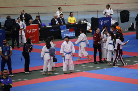 Martial arts competition with athletes in white gis on a red and blue mat, officials and spectators in the background.