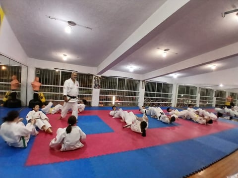 Group of children in white martial arts uniforms practicing on a red and blue mat in a gym with an instructor