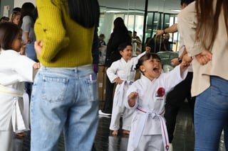 Niño con cinturón rosa rodeado de adultos en evento de karate