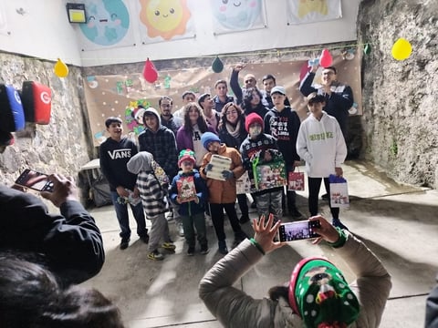 Group of children and adults celebrating at a birthday party in a concrete room with colorful decorations and balloons