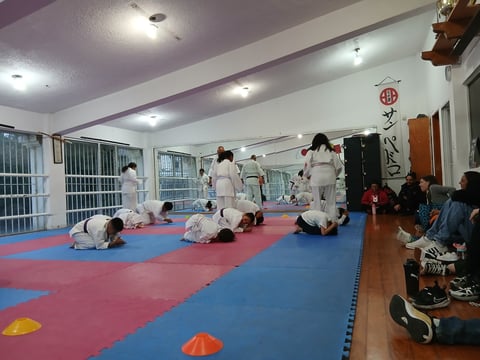 Children in white uniforms practicing martial arts or judo on a red and blue padded mat in a training hall