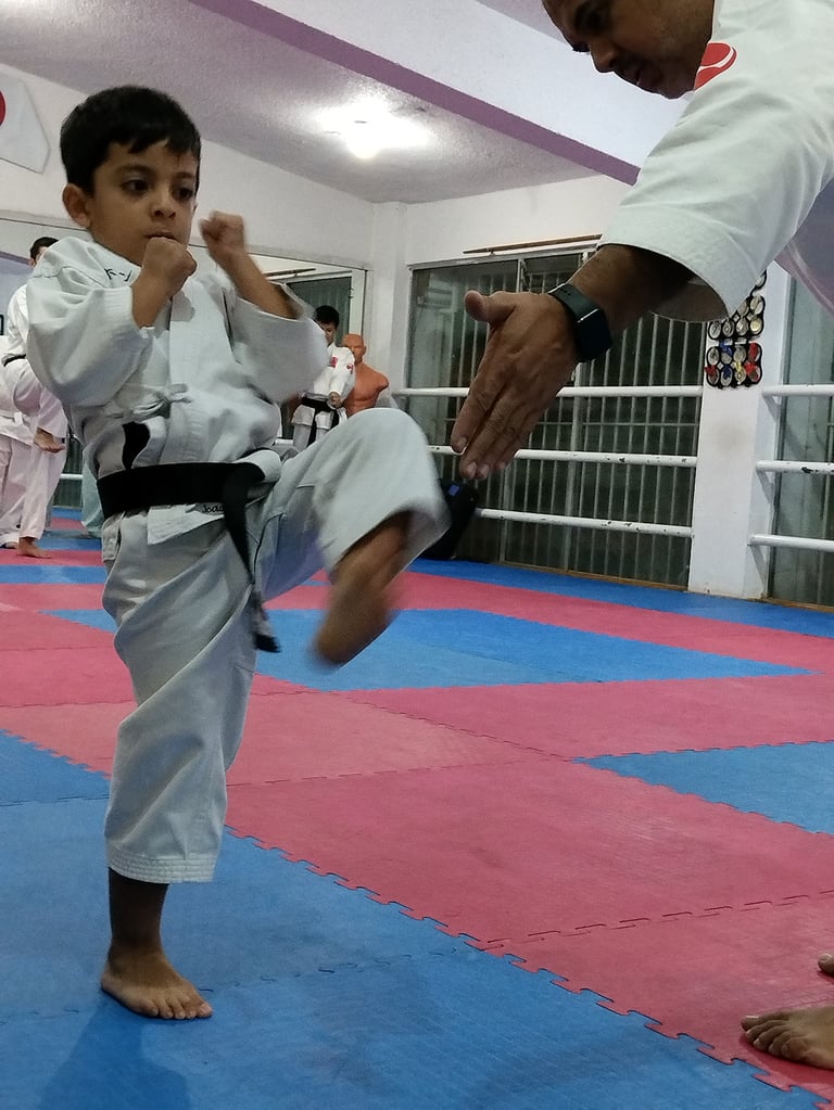 Young child in white karate gi performing a high kick during training with instructor in gym