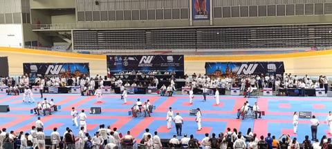 Large indoor karate tournament with athletes in white uniforms competing on blue and purple mats in an arena