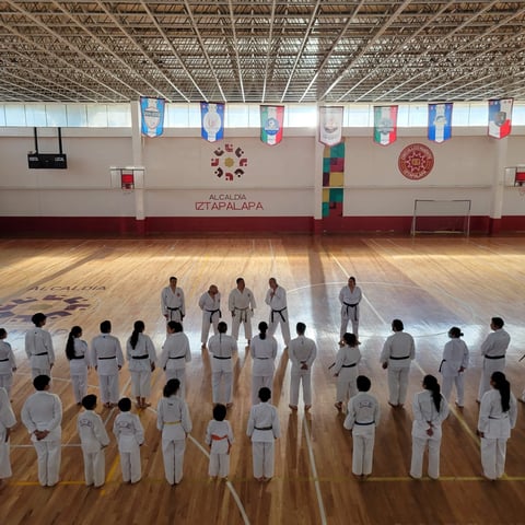Group of karate students in white uniforms standing in rows on a wooden gym floor during training session
