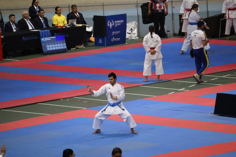 Karate competitors in white gis on blue and red mat during tournament with judges and spectators watching