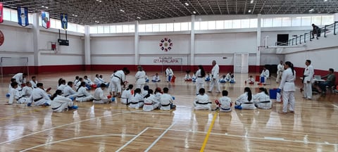 Large group of people in white martial arts uniforms practicing together in a gymnasium during a training session or class
