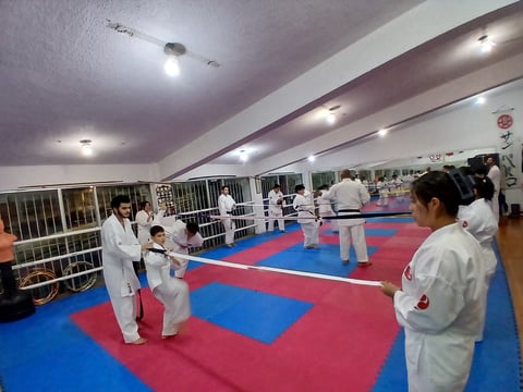 Martial arts training class with students in white uniforms practicing on a red and blue mat in an indoor dojo