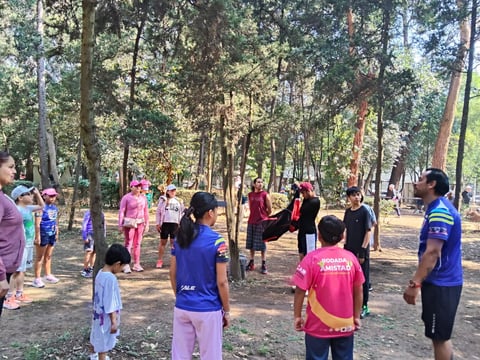 Children and adults participating in outdoor activities and games in a shaded forest park setting