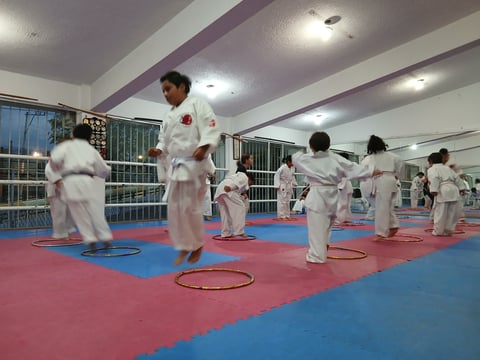Karate class with instructor and children in white gis training on red and blue mat floor