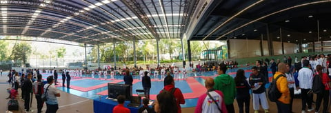 Indoor sports facility with colorful court floors and many spectators and participants gathering under a covered structure