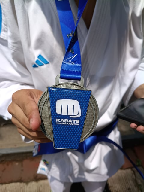 Person in white karate gi holding a blue and silver karate medal with blue ribbon