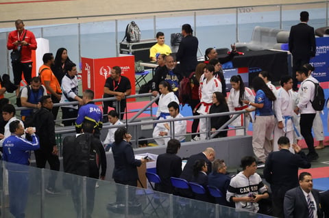 Young martial artists in white uniforms competing at an indoor judo or karate tournament with spectators and officials present.