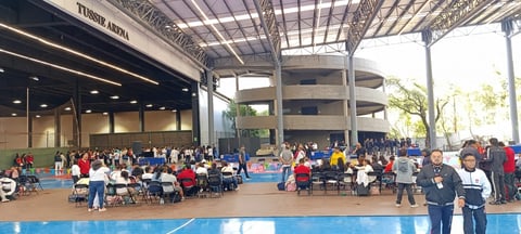 Indoor sports arena with large crowd of athletes and spectators gathered on blue court during a competitive event