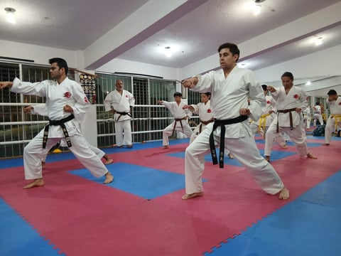Group of martial artists in white karate uniforms practicing on a red and blue mat in a dojo training facility