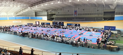 Indoor sports arena with large crowd watching martial arts competition on multiple blue and purple mats