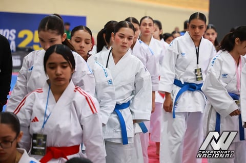 Group of young female karate competitors in white gis with colored belts standing together at a competition event