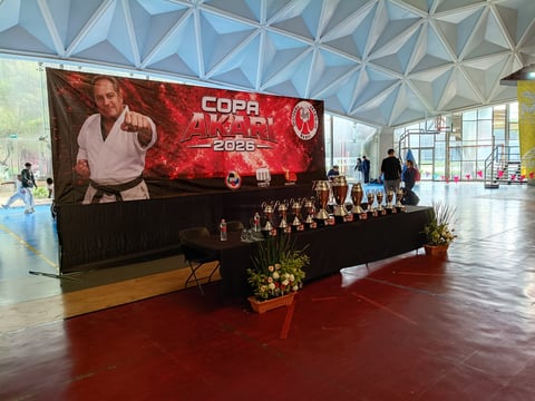 Indoor event space with a large red COPA 2026 banner displaying a martial artist, trophies on a black table, and geometric ceiling