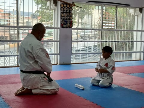 Martial arts instructor in white gi kneeling and teaching a young student in dojo with blue and red mat