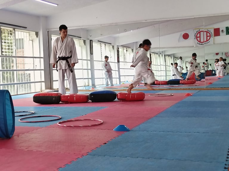 Martial arts class in a dojo with students in white uniforms practicing on a red and blue mat with training equipment